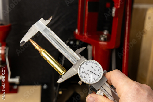 Precision measurement of a rifle cartridge with a dial caliper, emphasizing accuracy and detail