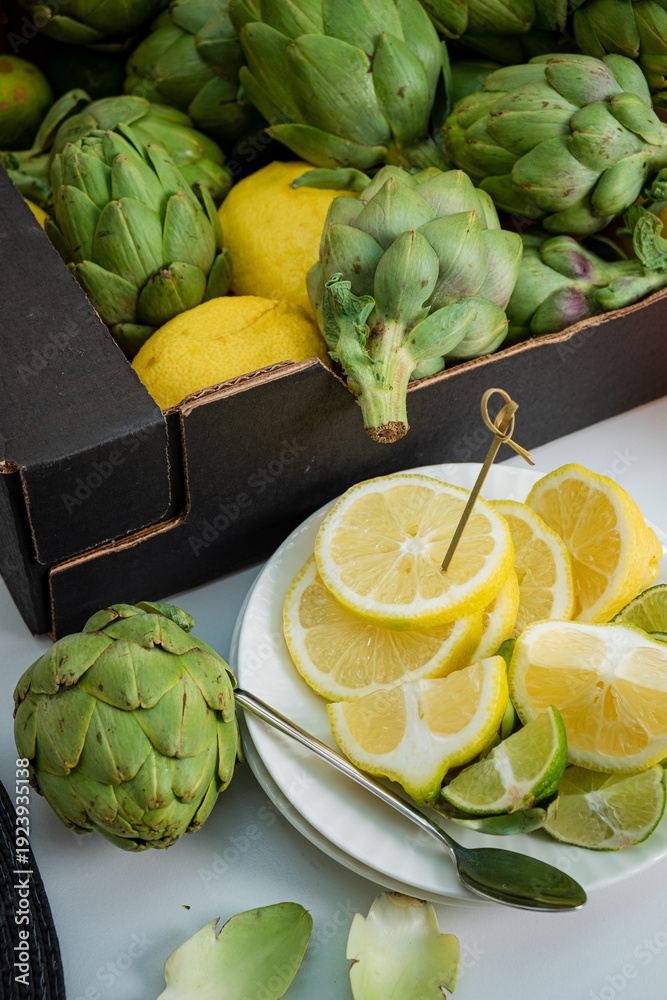 Naklejka premium A plate of lemon slices and a fresh artichoke beside a box of artichokes and lemons
