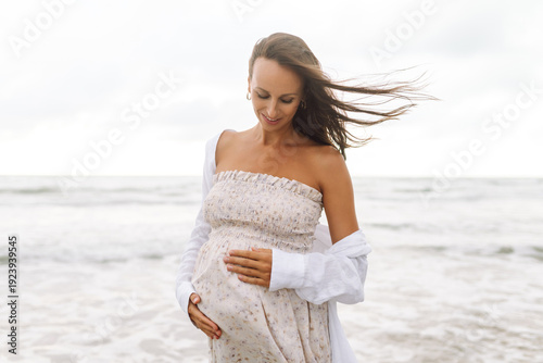 Quadro su tela A young pregnant woman walks along the beach, enjoying the seascape