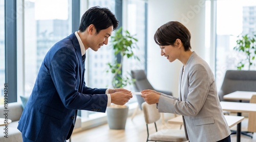 モダンな会議室で名刺交換をする日本人男性社員と女性社員