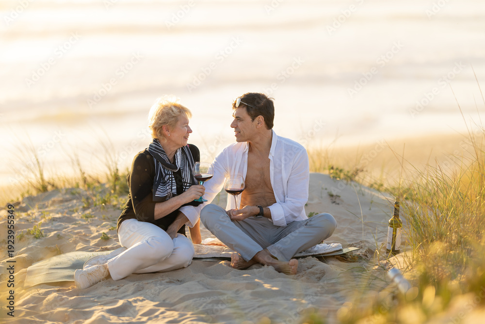 Fototapeta premium Couple enjoying wine on a sandy beach at sunset