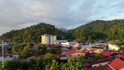 Aerial view of Pulau Pangkor village, morning sunlight casting golden glow across rooftops and turquoise waters.