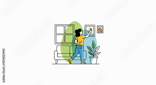 Woman arranging framed pictures on wall with sofa and plant