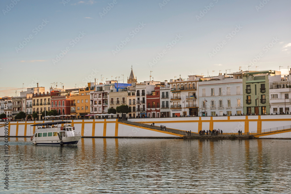 Obraz premium Tourist Boat Passing Colorful Riverside Houses in Triana, Seville