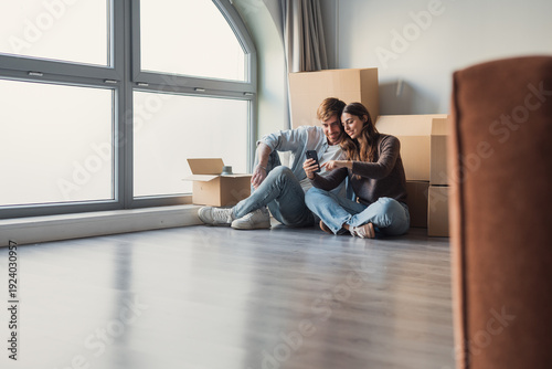 фотографія A smiling couple relaxes after moving into a new apartment, sitting near boxes a