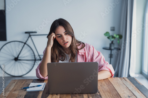 Cuadro en lienzo An overworked woman sits at her workspace beside a laptop, pressing her hands to