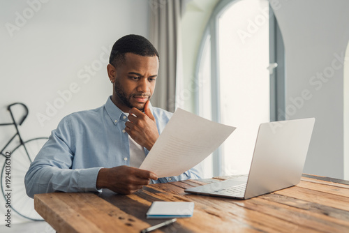 Fotografia Concentrated African American manager reading letter, paper handout, analyzing company statistics, thinking about financial risks, comparing results