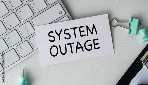 Photos System Outage text on business card near computer keyboard