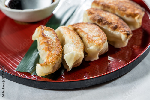 Fotografie A red plate with golden brown pan-fried dumplings served with soy dipping sauce on the side