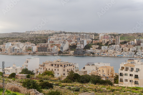 View of buildings of various sizes and shapes dominate the landscape with the ocean nearby under a cloudy sky, Malta.