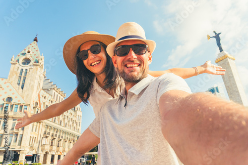 Happy young couple taking selfie in front Batumi europe square traditional city buildings. Two tourists having fun on romantic summer vacation in Georgia - Holidays and traveling lifestyle concept