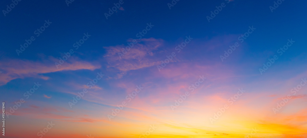 Obraz premium Beautiful sunset sky with orange and blue gradient clouds background,A stunning panoramic view of the twilight sky during sunset, featuring a vibrant gradient of deep blue, purple, and golden orange 