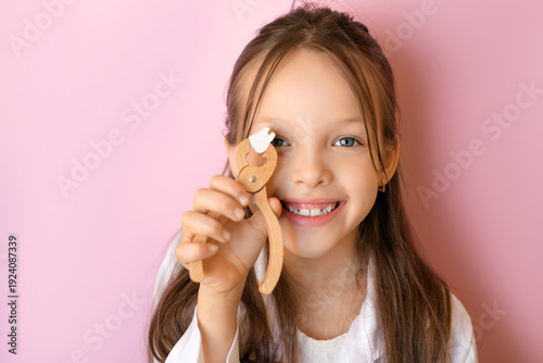 Bilde på lerret A cute funny girl holds dental forceps and a tooth