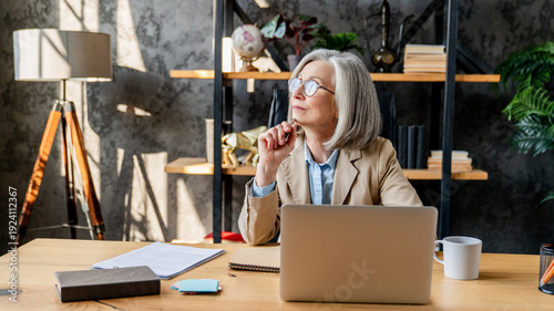 Middle-age woman using laptop computer for business studying, having videocall with online virtual webinar training meeting, writing notes. Focused businesswoman working in office. Copy space