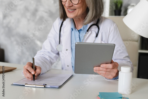 Doctor writing medicine prescription on clipboard and working on desktop computer pc tablet at doctor's office in hospital, treatment plan. Doctor working at office, filling insurance document