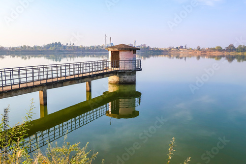 Tableau sur toile A serene morning view of a calm lake in Davanagere with a small pump house reflecting on the water's surface