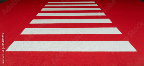 A zebra crossing with a red background and white stripes for crossing the road.