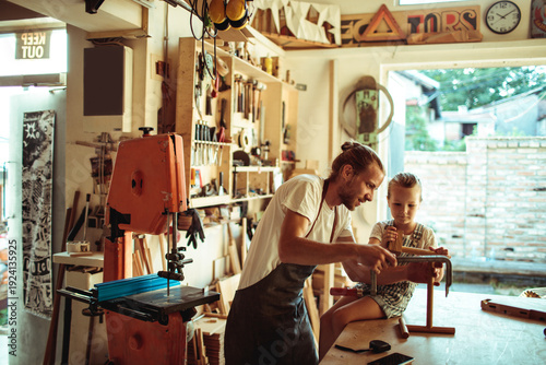 Carpenter teaching child woodworking in home workshop
