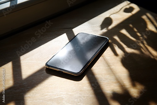 Smartphone placed face down on wooden surface near window with sunlight casting shadows and reflections, creating a serene indoor atmosphere