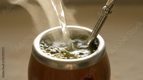 Preparing traditional yerba mate drink sequence. Hot water pours into bamboo gourd with bombilla, creating steam.