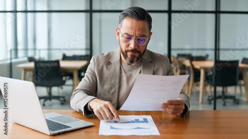 Businessman analyzing financial documents at office desk with laptop