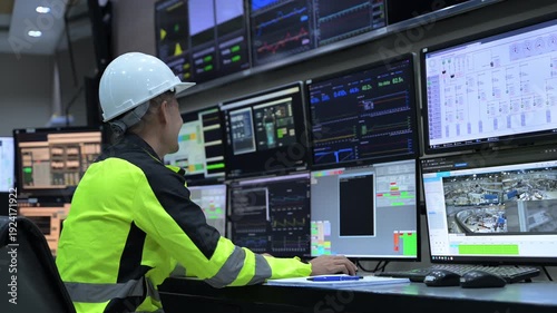 Professional engineer monitoring complex data systems on multiple screens in modern control center. Male worker analyzing digital charts and graphs for security and automation performance.