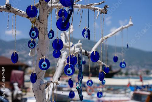 Colorful nautical-themed jewelry. Nazar amulet pendants sway against port landscapes. Elegant Blue Eye amulets hang delicately from sunlit white branch. Amulets against evil eye in Turkic countries