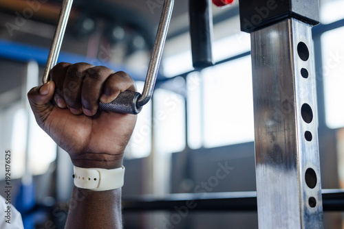 African American man gripping knurled V-handle on cable in gym, tee near support post, copy space