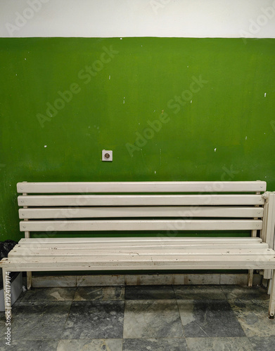 A white bench set against a green wall in a waiting hall.