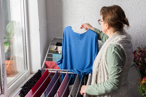 Canvastavla A woman around 50 years old is hanging clothes on a drying rack outside her balcony