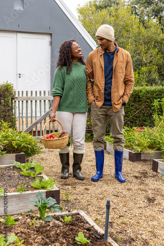 African American couple walking arm-in-arm through backyard garden holding woven basket with tomato