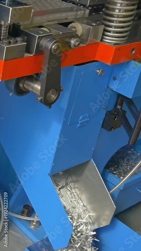 Industrial automatic sheet stamping machine actively forming metal sheets. A stream of small, gleaming metal offcuts cascades into a collection chute.