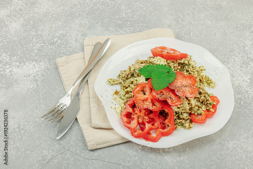 Plate of mafalda corta pasta with basil pesto, fresh tomatoes and herbs. Vegan healthy meal concept