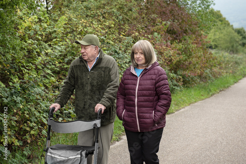 Elderly friends taking a walk in the park with help of walker to support and help move smiling and talking happy