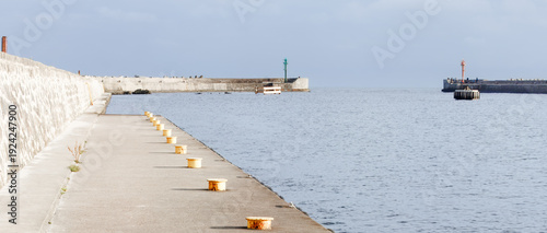 Foto Baltic shore legacy concrete breakwater walkway with mooring bollards leading toward harbor entrance in Ustka Pomerania Poland for coastal infrastructure documentation and northern seaside travel use