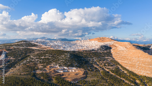 The majestic appearance of the marble quarry on a cloudy day. The contrasting overall view of the reforestation at the foot of the mountains and the mining area.