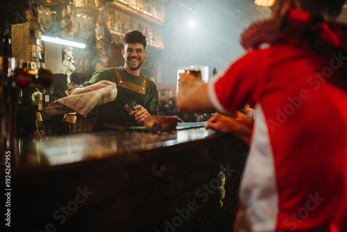 Billede på lærred Friendly bartender serving customer at busy pub