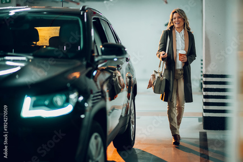 Professional woman arriving at or leaving her car in a modern underground parking garage, holding coffee and a car key