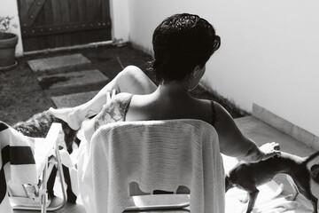 Black and white photo of a woman sitting on a chair in a sunny patio