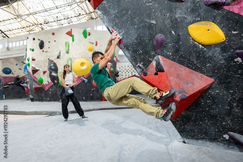 Man bouldering at indoor climbing gym, woman watching