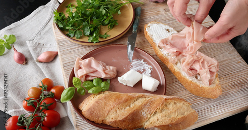 Slika na platnu Anonymous person prepares sandwich with cheese, basil, and mortadella in kitchen