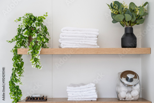 Minimalist Bathroom Interior with White Towels and Toiletries on shelf with greenery on white background
