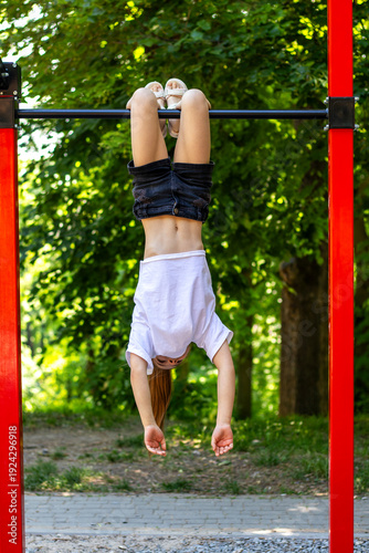 Girl hanging upside-down from playground bar on a summer day enjoying playful outdoor fun