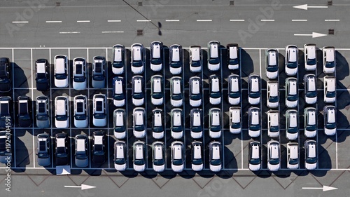 Aerial view of neatly arranged rows of cars in a parking lot, light reflecting off their roofs, casting long shadows on the asphalt, Civitavecchia, Lazio, Italy.