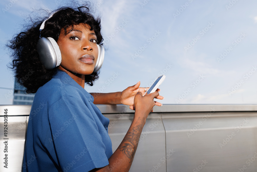 © Artem Podrez/Stocksy - Portrait Woman Holding Phone with Headphones Sky Background © Artem Podrez/Stocksy - Portrait Woman Holding Phone with Headphones Sky Background