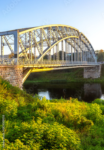 View on the steel arch bridge across the Msta river in summer in sunset light. Built in 1905. Borovichi, Russia