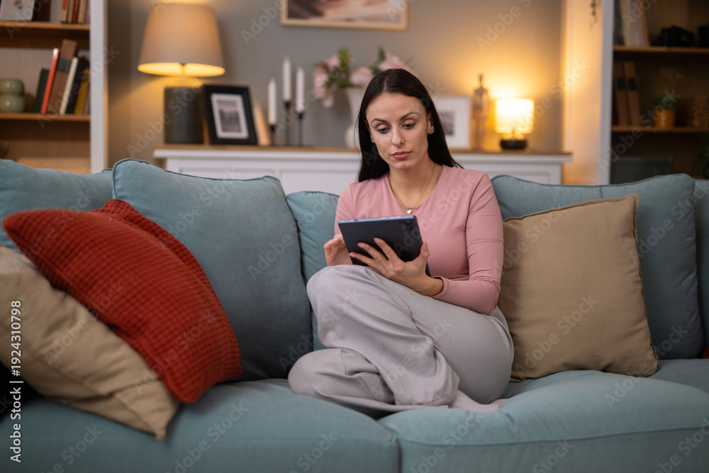 Obraz premium Woman relaxing at home, using tablet on sofa
