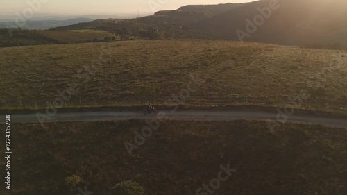 Vista aérea de uma mulher pilotando uma motocicleta em uma estrada de terra deserta no alto da montanha no nascer do sol