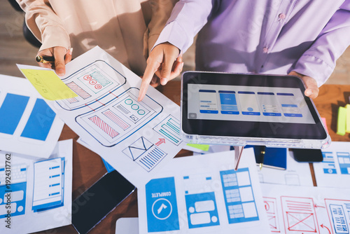Close up ux developer and ui designer brainstorming about mobile app interface wireframe design on table with customer breif and color code at modern office.Creative digital development agency.