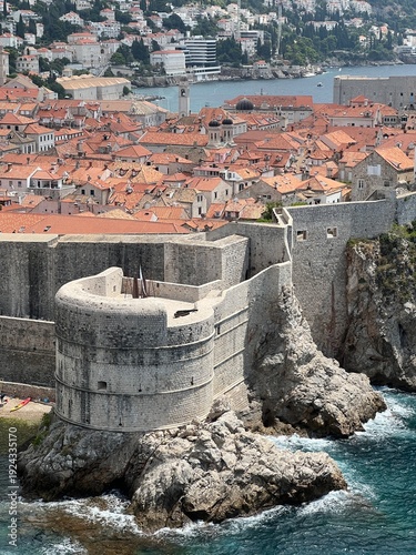 Zoomed top view of Bokar Bastion standing on cliffs with red roofs of Dubrovnik old town in back, waves crashing on rocks, summer time, august, Dubrovnik, Croatia